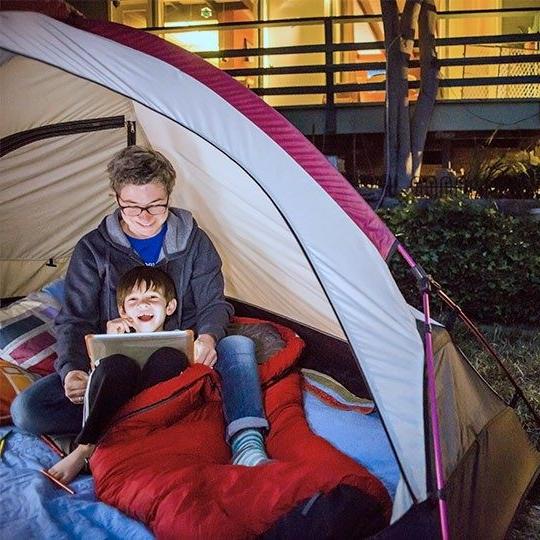两个男孩在自家后院的一个帐篷里，通过固定的无线网络在平板电脑上播放内容