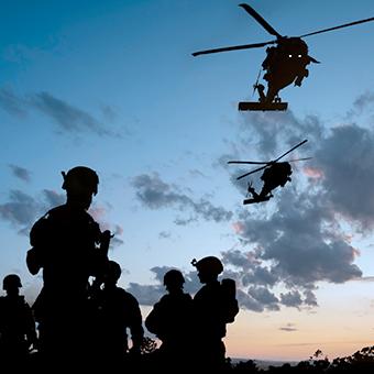 黄昏时分，五名军人的剪影在战场上，两架直升机在上空飞行