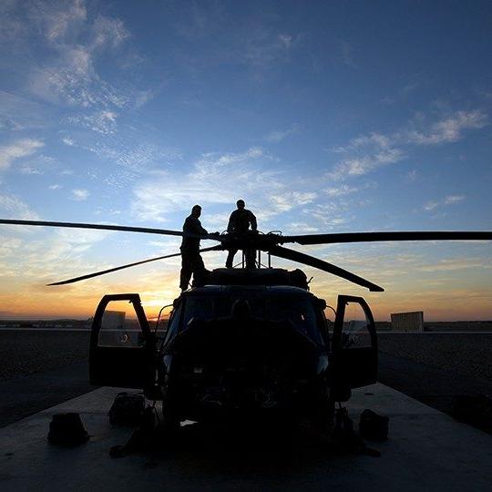 日落时分，两名战士在一架直升机上检查旋翼