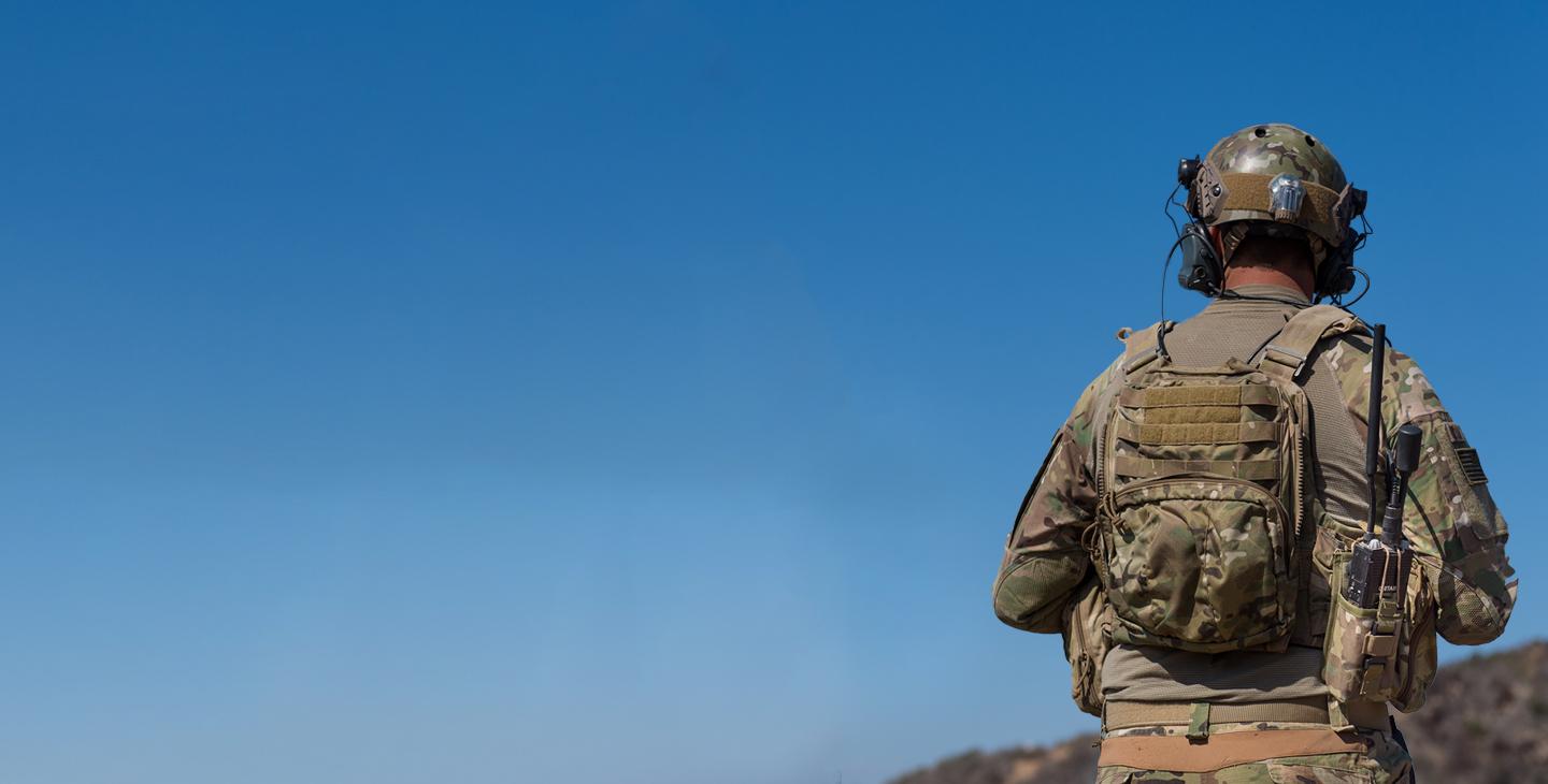 一名士兵身穿绿色迷彩战斗制服，背包上装有无线电