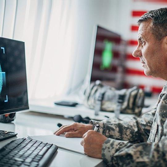身穿军装的男子一边在纸上写字，一边看着电脑，电脑上有一个受ecrypt保护的硬盘驱动器