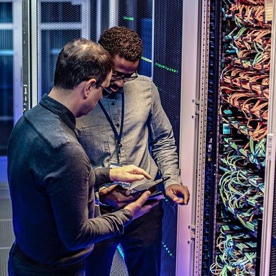 两个男人在服务器室边看平板电脑边讨论数据保护