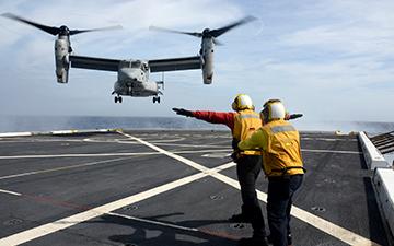 两名机组人员正在帮助一架军用飞机在海上的一艘船上降落