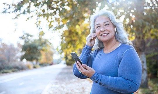 一名女子戴着苹果耳机站在树前用家庭网络电话聊天