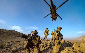 三名士兵在战场上警戒，一架直升机在上空飞行